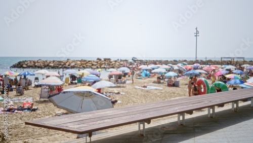 Bild auf Leinwand Boardwalk bench in sharp focus with blurred beach umbrellas and shoreline bokeh, outdoor; background backdrop copyspace calm