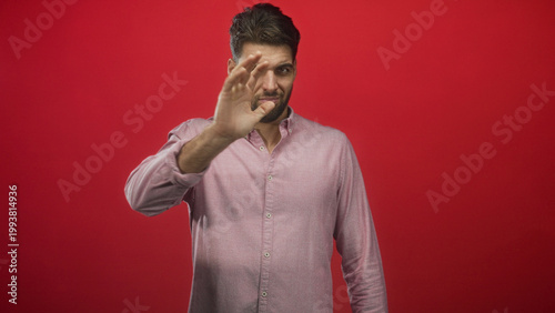 Foto Hispanic man with beard covering face with hand in studio against red backdrop; embarrassment privacy