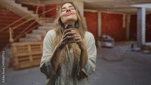Foto Middle age woman holding coffee cup with hands and closed eyes in unfinished building renovation site; calm reflection