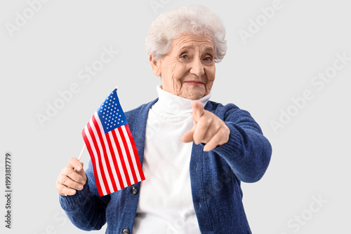 Photos Senior woman with USA flag pointing at viewer on light background