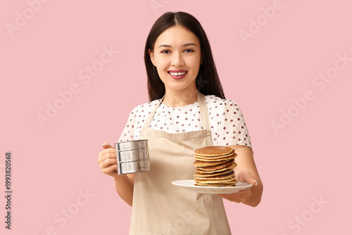 Young Asian woman with tasty pancakes and metal mug on pink background