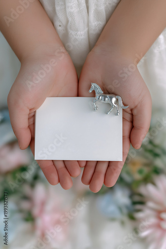 Child's hands hold a blank card with a small silver horse figurine on the edge