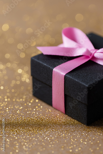 Elegant black gift box with pink ribbon on a sparkling gold background