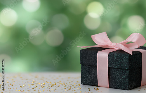 Elegant gift box with pink ribbon on a white surface with bokeh background