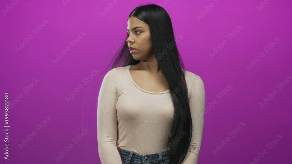 Naklejka premium Young latin woman clutches chest and gazes sideways in studio setting with purple backdrop; anxiety.