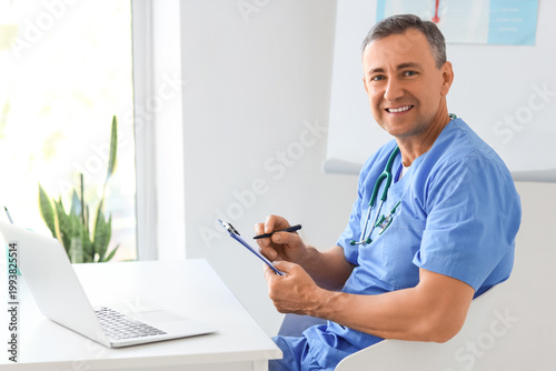 Mature doctor working with clipboard at desk in medical office