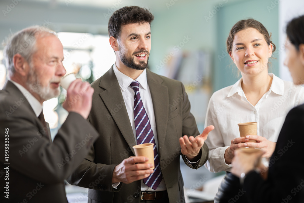 © JackF - Group of positive office workers drink coffee and chat during work break in office of large business company