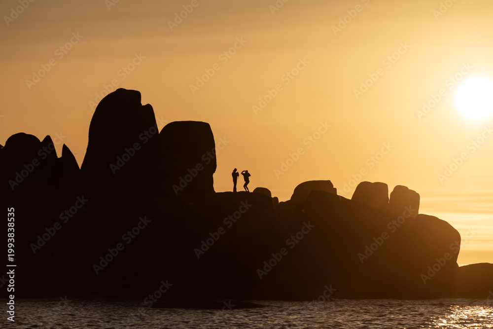 Obraz premium Rock formations silhouette with couple standing during sunset creating scenic coastal dramatic landscape view