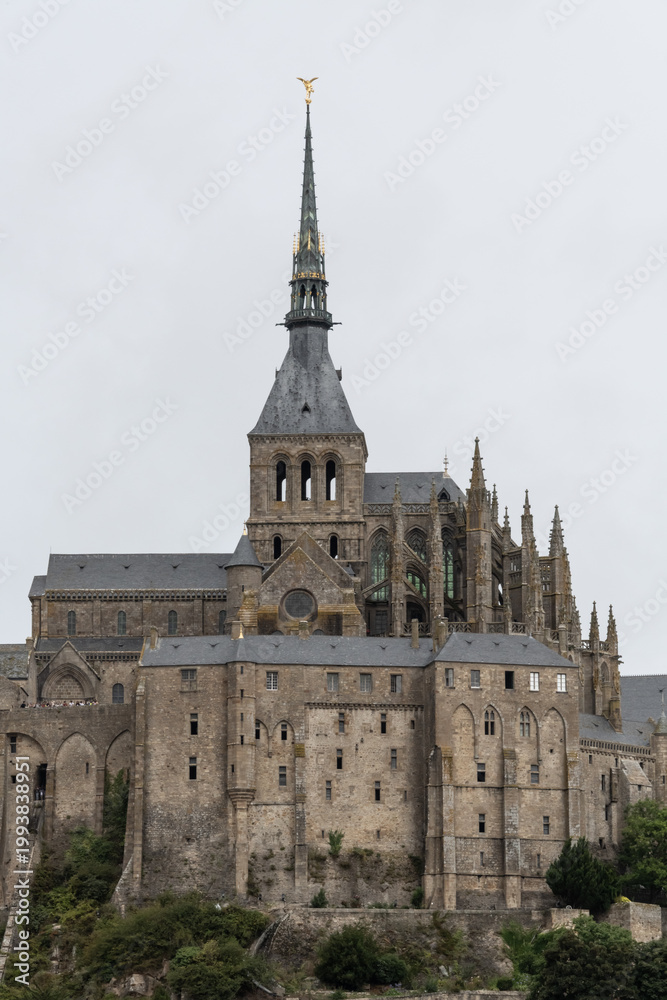 Obraz premium Mont Saint Michel abbey rising above landscape with historic architecture and cloudy sky background