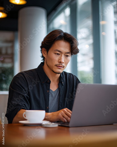 Stylish East Asian man in his early 30s working on laptop in a modern cafe