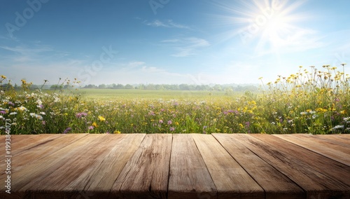 Empty wooden table overlooking vibrant sunlit wildflower meadow under bright blue sky