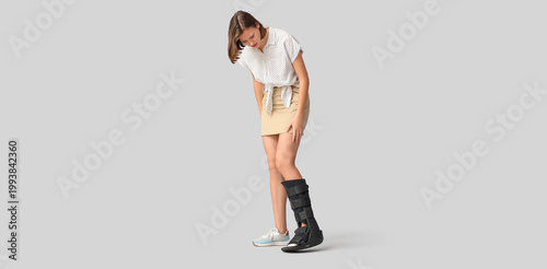 Young woman with broken leg on light background