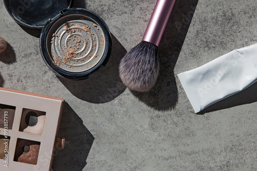 A flat lay of makeup tools, including an open compact with powder remnants on grey surface