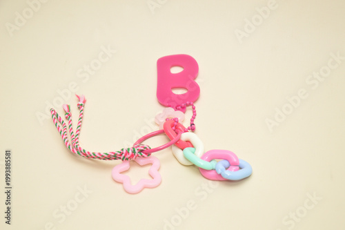 Pink plastic letter B keychain with star and flower charms. Colorful toy accessories for kids fashion, school bags, and creative decorations on beige background.