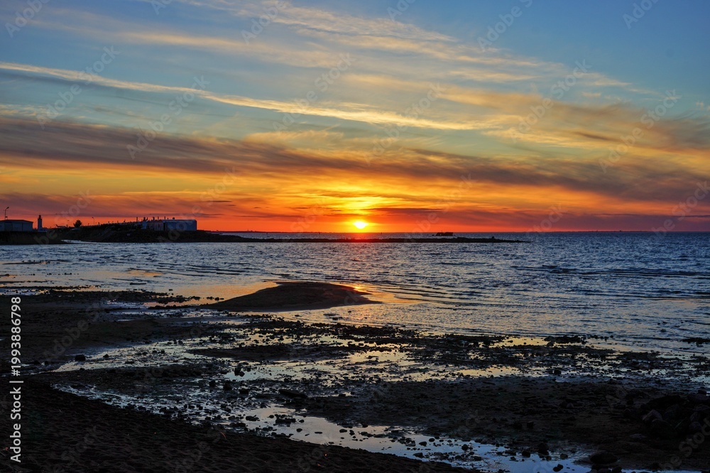 Fototapeta premium A picturesque view of the setting sun with clouds. A calm sunset over the Gulf of Finland, tinged with warm tones.