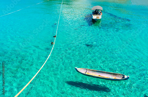 Beautiful tropical atmosphere of Atauro beach in Timor Leste, featuring fishing boats floating on crystal clear turquoise waters where children swim and play.