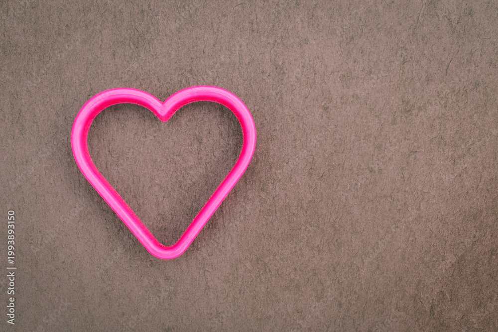 Fototapeta premium Bright pink heart shape rests on a gray surface near the edge during daytime