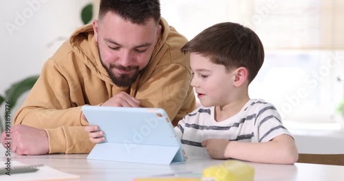 Father and his son using tablet at white table indoors