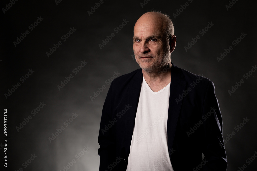 Fototapeta premium Bald middle aged man in a dark suit jacket and white t shirt posing with a serious expression