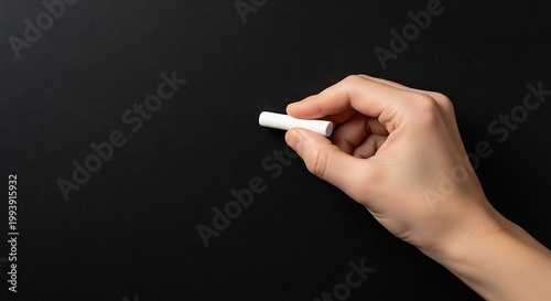 Hand holding chalk ready to write on black chalkboard