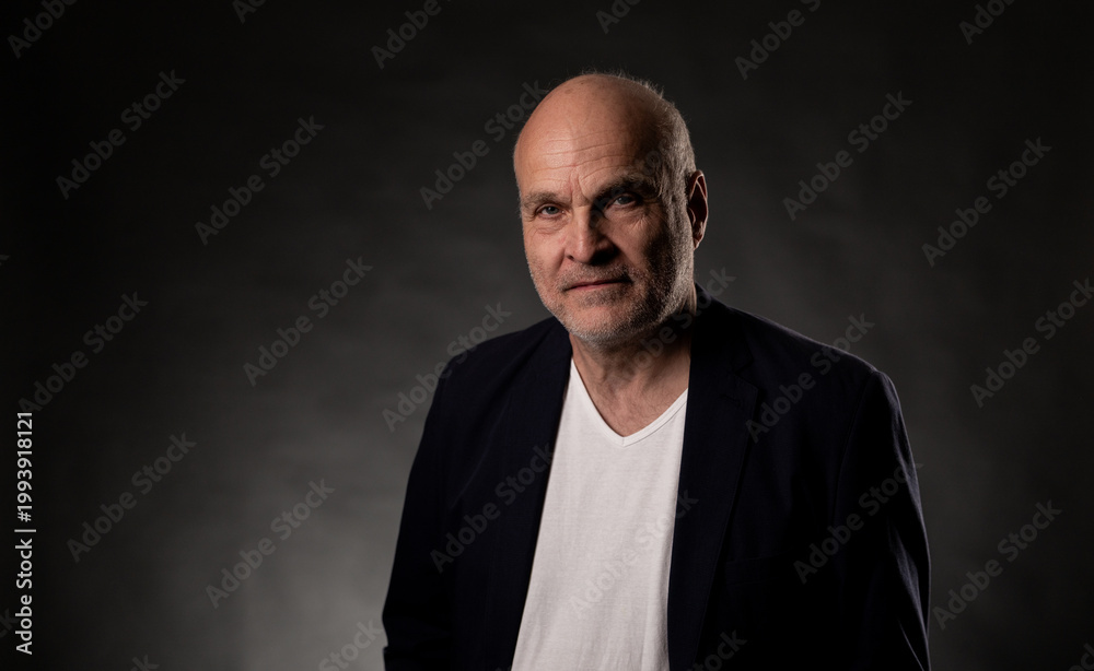 Fototapeta premium Volker Schlondorff, an aging bald man, is posing for a portrait in a studio