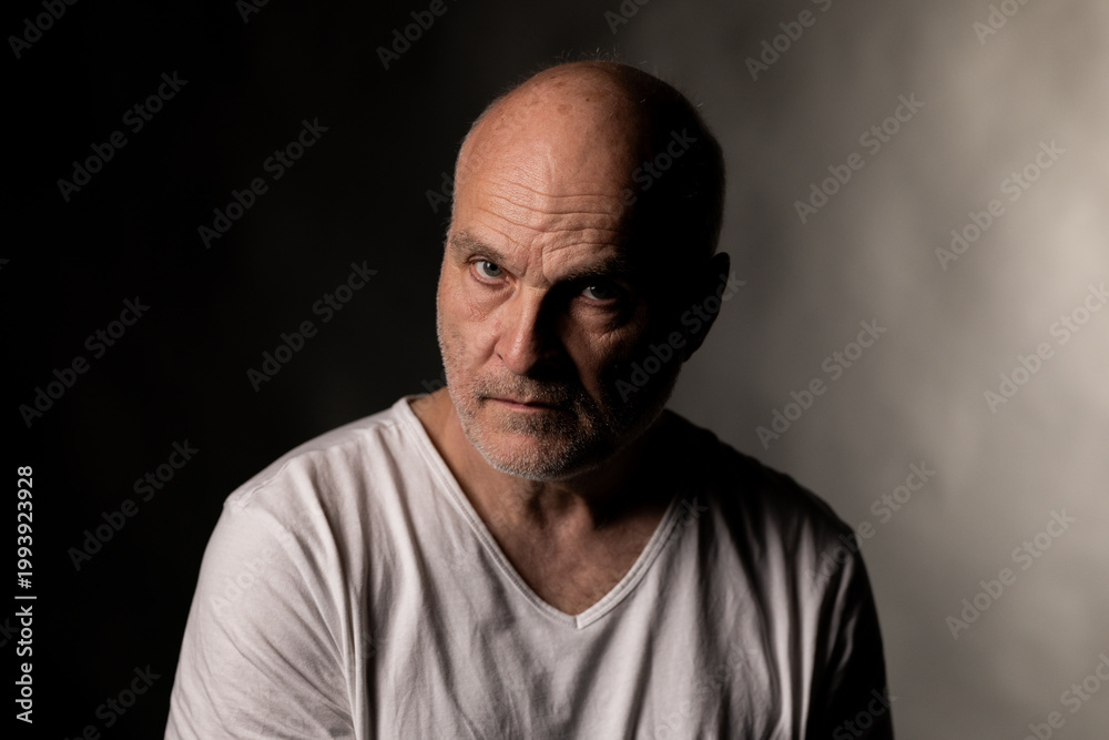 Fototapeta premium Older man's portrait with baldness, a serious expression, and stark dramatic lighting