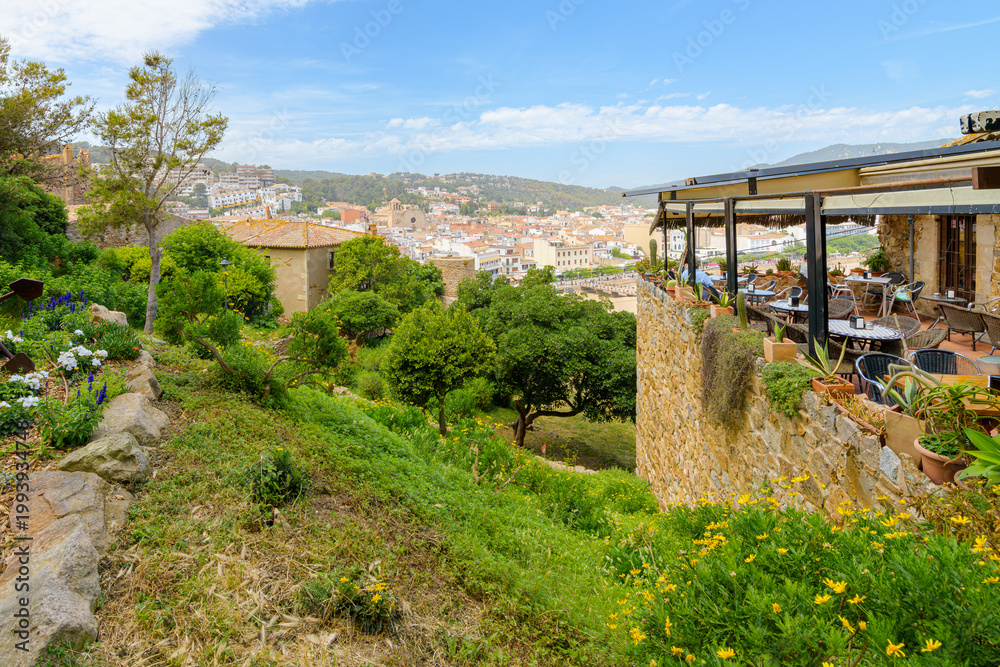 Fototapeta premium The terrace of a restaurant inside the walls of the 12th century castle, with views of the whitewashed village and sandy beach of Tossa de Mar, Spain.