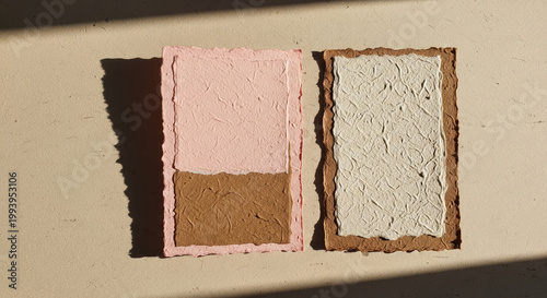 Rustic flat lay of two handmade textured paper cards with pink brown and cream colors casting shadows on a beige surface
