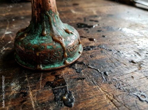 A close-up view reveals an antique oxidized copper object with green patina and drips resting on a dark, wet wooden surface.