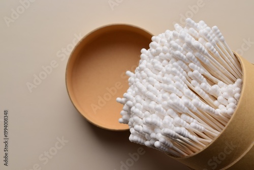Close-up of a cardboard tube with cotton swabs on a beige background. Pile of cotton swabs for hygiene