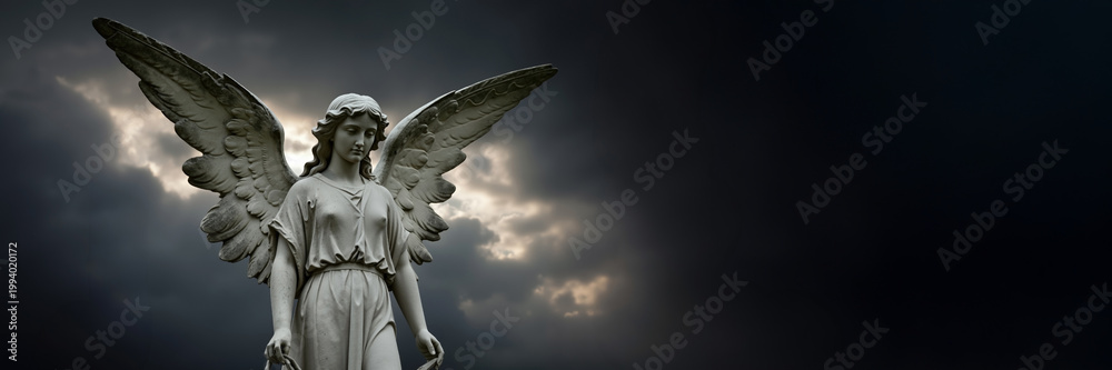 Naklejka premium Weathered stone angel statue with large wings stands against dramatic dark sky. Spiritual concept of grief, faith, and mourning. Panoramic banner with copy space