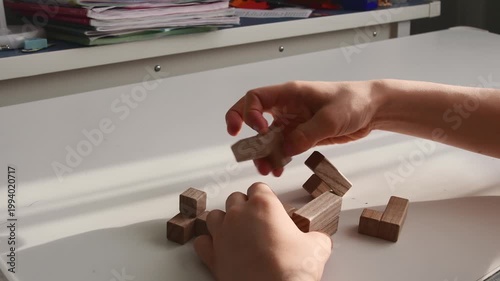 Close-up of hands solving a wooden 3D logic puzzle on a white desk. Concept for problem-solving and strategy