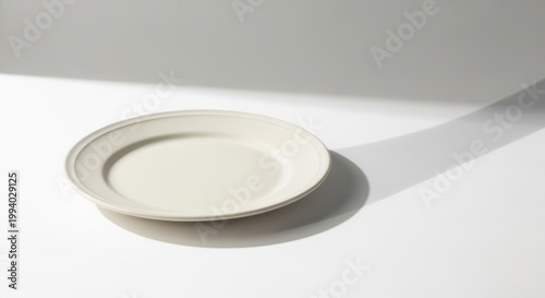 Minimalist food photography A pristine, bone-white plate with soft shadows on a white surface. Simple, elegant, modern kitchenware in studio setting.