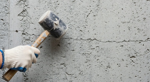 Worker holding a rubber mallet against a cracked concrete wall