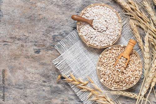 Top view of natural barley grains in small woven baskets with wooden scoop, placed on a rustic wooden table. Surrounded by dried barley ears and a linen cloth.