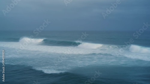 Ocean waves crash on shore under cloudy skies with white foam forming