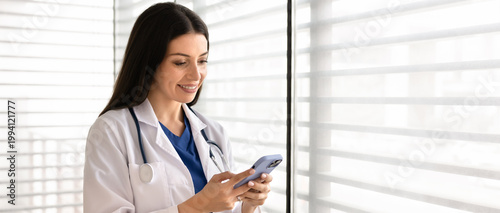 Banner of female doctor standing in clinic office, holding smartphone, checking medical information. Concept of digital healthcare, telemedicine, online consultation, remote patient communication