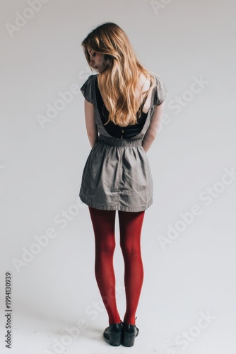Young Woman In Grey Dress And Red Stockings Standing Against A White Background