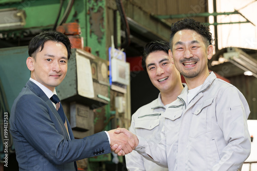 製造業の工場で握手する営業マンと作業員の信頼関係ビジネス契約や合意シーン　業務提携、協力、融資などのbtobの法人営業イメージカメラ目線