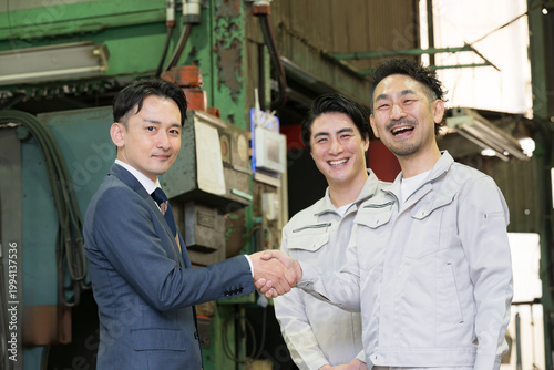 製造業の工場で握手する営業マンと作業員の信頼関係ビジネス契約や合意シーン　業務提携、協力、融資などのbtobの法人営業イメージカメラ目線