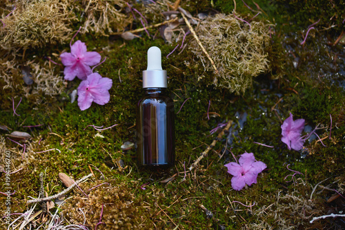 Natural skincare serum bottle surrounded by pink flowers and moss