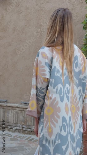 Woman in Uzbek robe opening carved wooden door in Tashkent old city