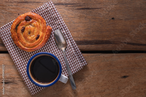 Cinnamon raisin roll and black coffee on rustic wooden table with copy space.