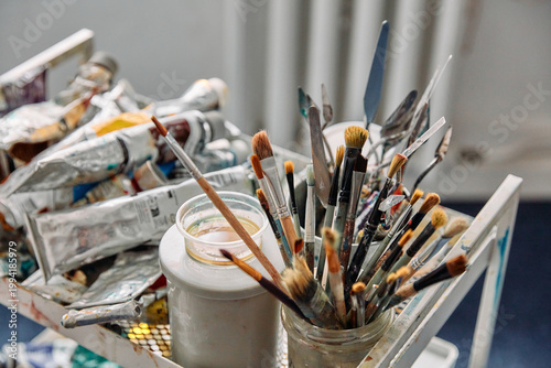 Artist brushes in a glass jar and tubes of oil paint in a creative studio setting