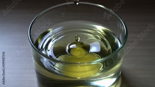 Close-up of a pickle submerged in a glass of clear liquid on a wooden surface with soft lighting.