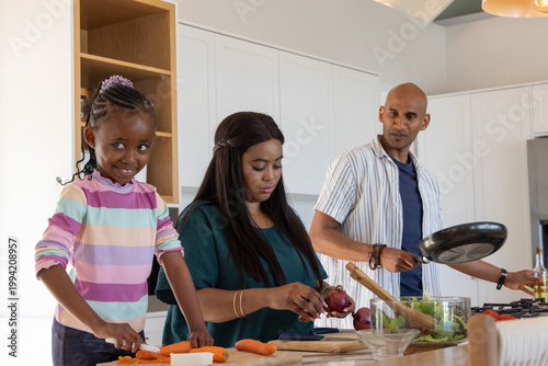 African American family chopping carrots, slicing red onion, holding frying pan at kitchen island