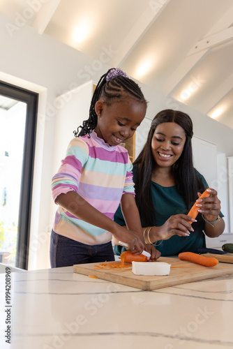 African American mother and daughter preparing carrots at kitchen island, peeling on cutting board