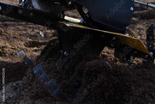 Walk-behind tractor attachment cultivating rich garden soil, preparing the ground for planting, ensuring optimal conditions for growing vegetables and crops in agriculture.
