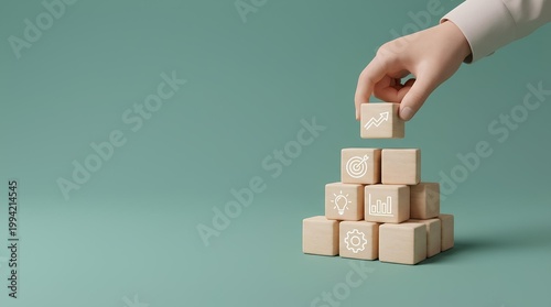 A minimalist 3D concept image showing a human hand placing a small wooden cube on top of a pyramid-like stack of cubes on a smooth muted teal-green surface