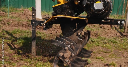 Male worker preparing the soil for planting by plowing the land with a walk-behind tractor in a garden on a sunny spring day, loosening the earth before sowing seeds for cultivation.